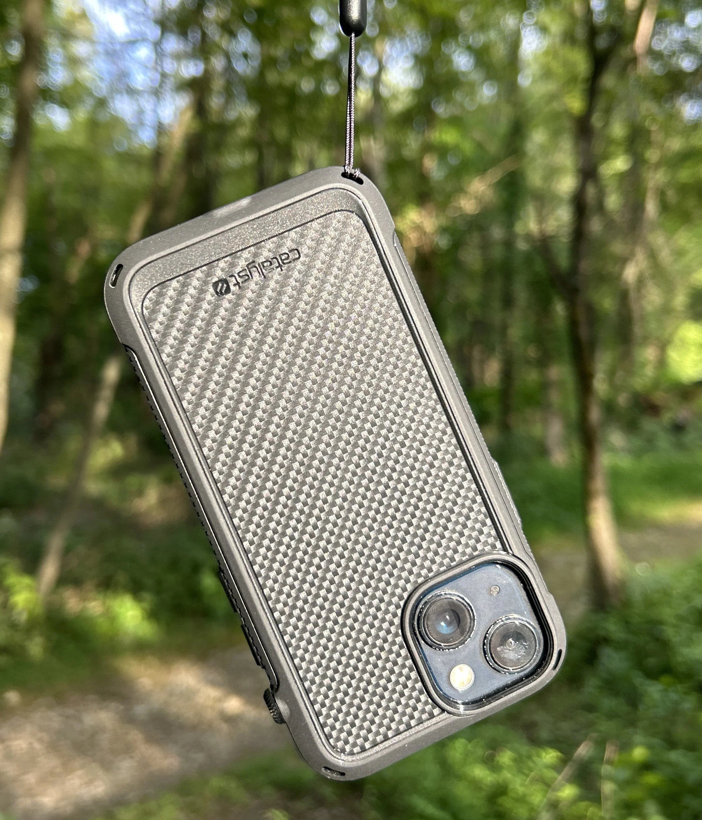 Catalyst drop proof protective iPhone case dangling from a wrist lanyard in the forest