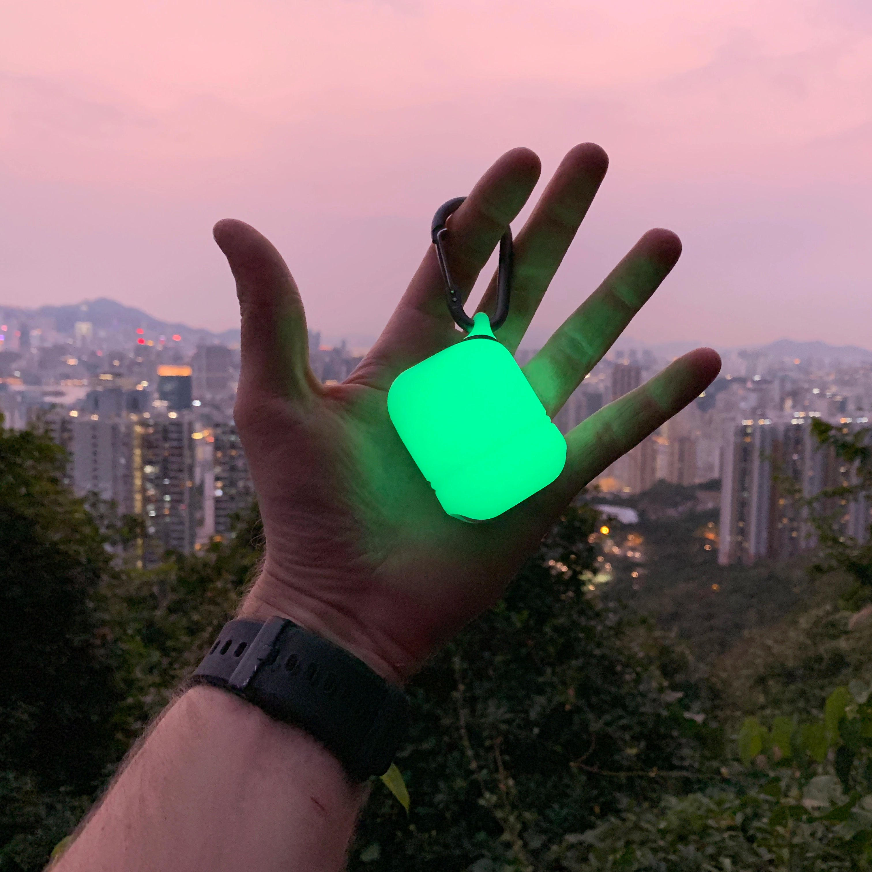 In a dusky cityscape, a person grasps Catalyst's Glow In The Dark AirPods (Gen 2/1) Waterproof Case, designed to ensure the AirPods remain secure.