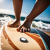 Person standing on a surfboard with feet visible, Airtags stuck on the foreground to the surfboard, ocean waves in the background