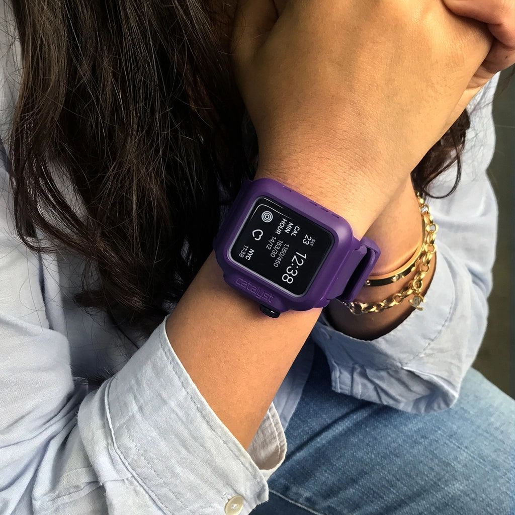 A person in a light blue shirt and gold bracelet rests their hand on their chin, wearing a purple Catalyst Waterproof Case for Apple Watch with a digital display showing 12:38.