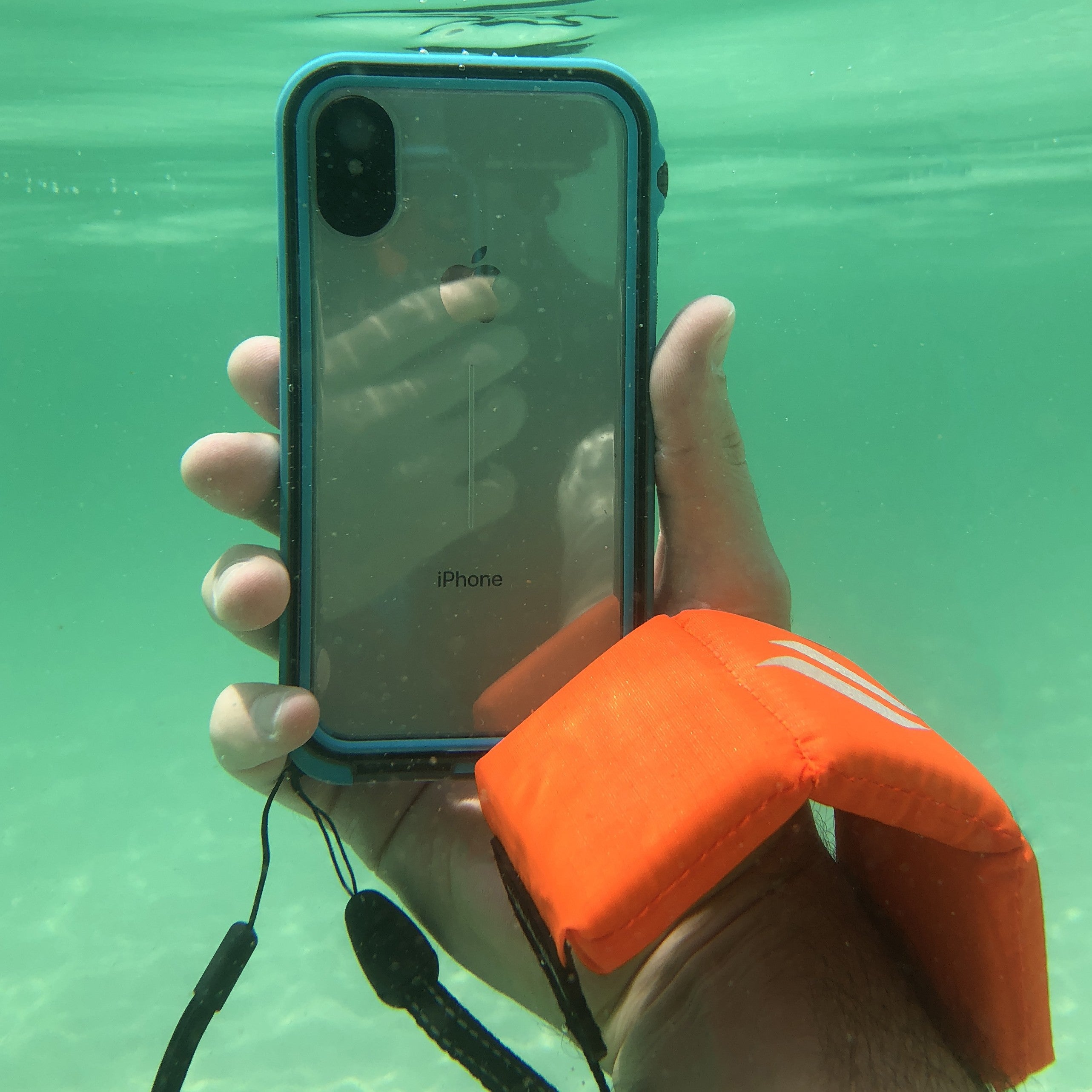 A hand grips an iPhone snugly encased in a Catalyst iPhone - Waterproof Case, Total Protection, in Glacial Blue. Expertly designed to keep water out, it's submerged underwater with a floating wrist strap for safe capturing of aquatic wonders.