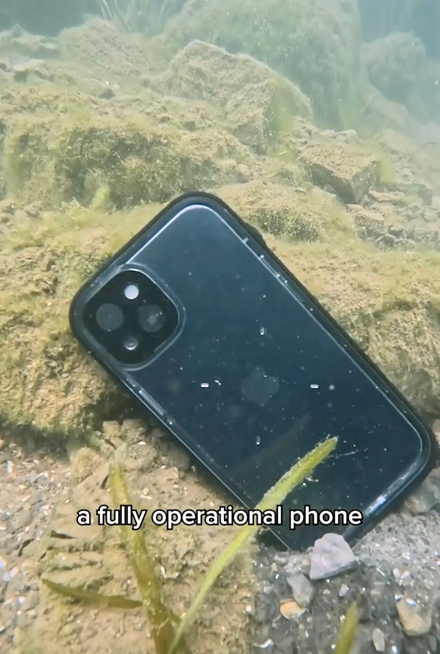 An iPhone 16 Pro in a Catalyst black waterproof case lies submerged on sandy terrain, surrounded by algae and pebbles. Text reads, "This fully operational phone seals out water, dust &amp; dirt.