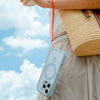 Woman holding a phone encased in the Sky Blue Drop Proof Case by Catalyst, attached to a wrist strap, carrying a woven bag against a backdrop of a cloudy sky.