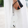 A person wearing a white dress holds a black wallet and a white smartphone with the Catalyst Drop Proof Case featuring an attached wrist lanyard.