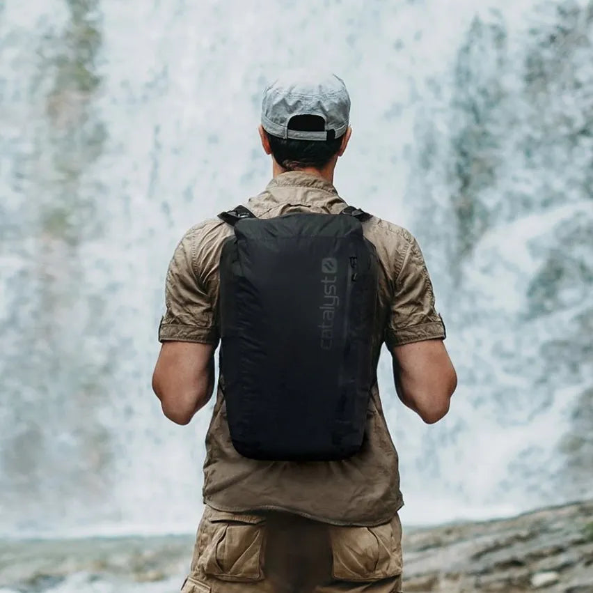 A man wearing the Catalyst 20L Waterproof Backpack walking towards a waterfall. 